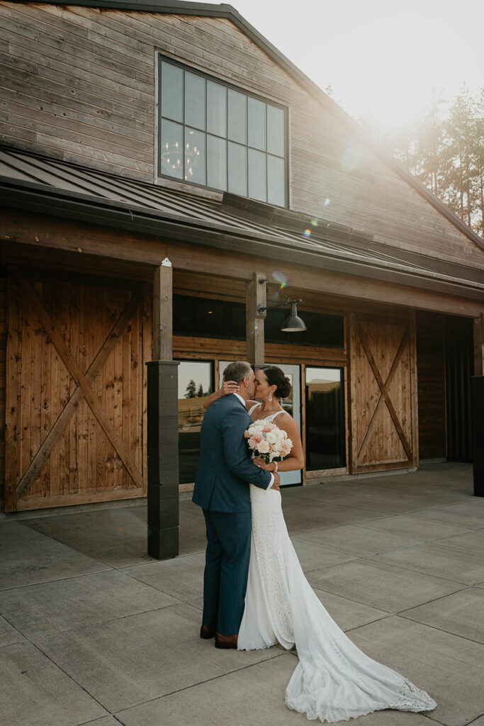 The bride and groom kissing by a wooden barn. 