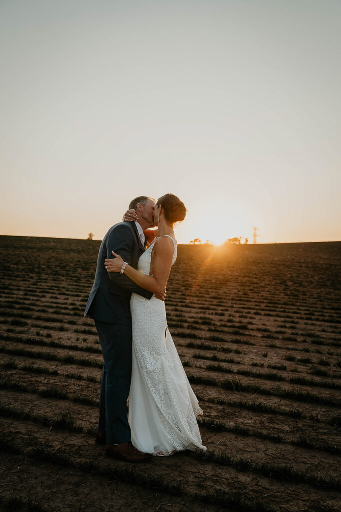 The couple kissing on a tilled farm at sunset. 