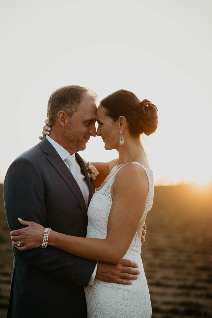 the bride and groom hugging on tilled farmland at sunset. 