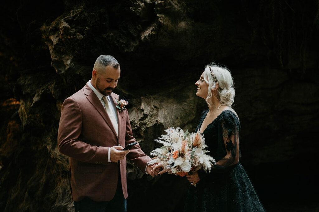 a couple holding flowers in front of a fallen tree trunk. 