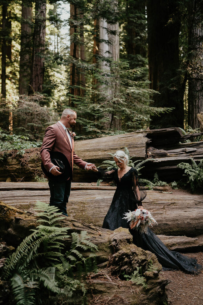 the husband helping his wife onto a fallen redwood trunk. 