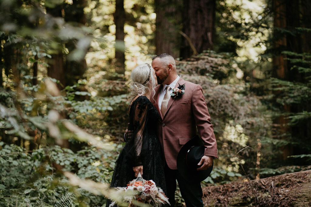 A couple kissing with California Redwoods around them.