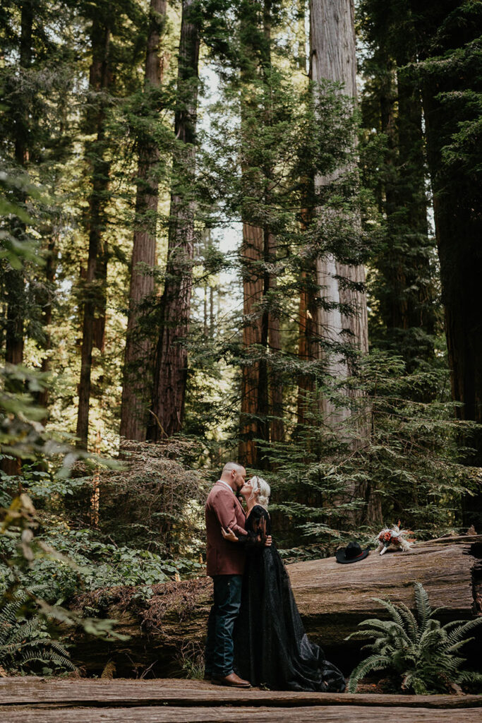 the husband and wife kissing in the middle of a redwood forest. 