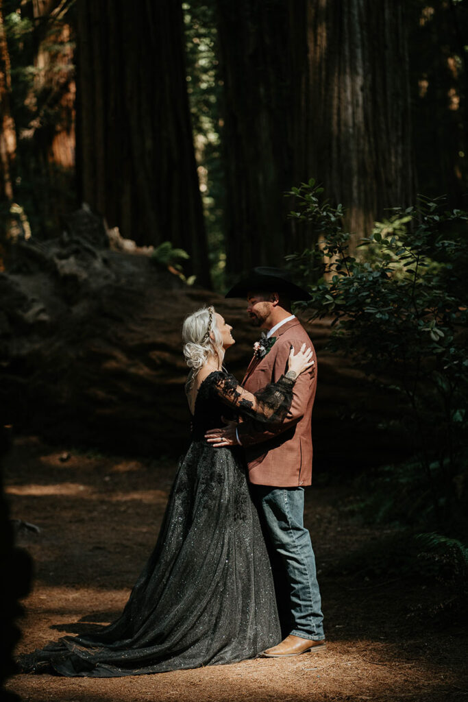 the newlyweds holding each other in the sunlight as it peers through the redwood forest canopy. 