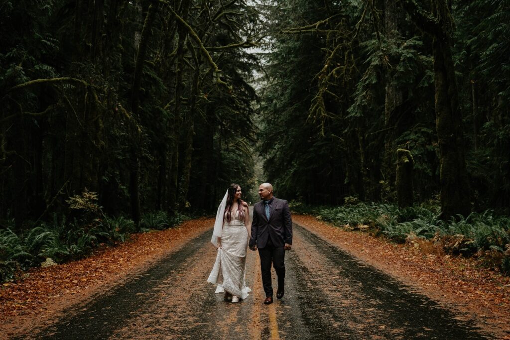 Bride and groom hold hands while walking down a street in the Hoh Rainforest during their elopement in Washington
