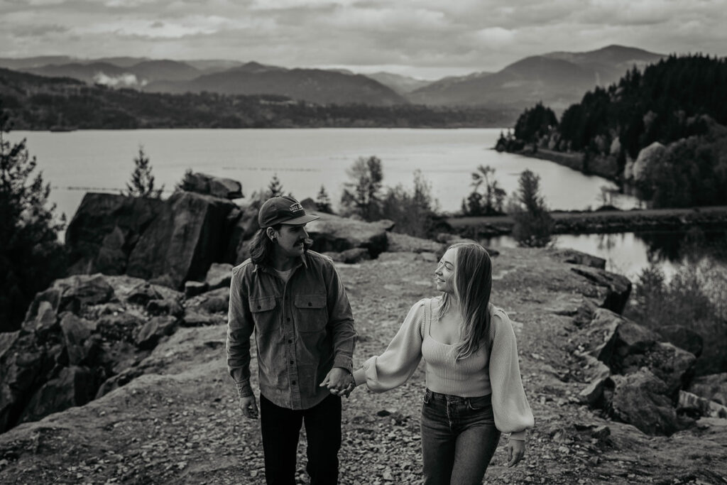 A couple holding hands and smiling at each other with the Columbia River Gorge in the background. 