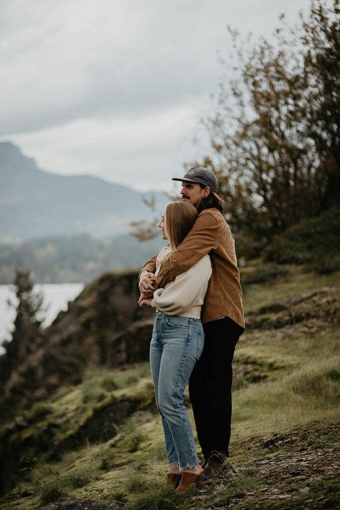 A couple holding each other standing on a river bank. 