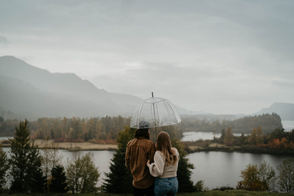 a couple cuddling under an umbrella during a gloomy day in the Columbia River Gorge. 