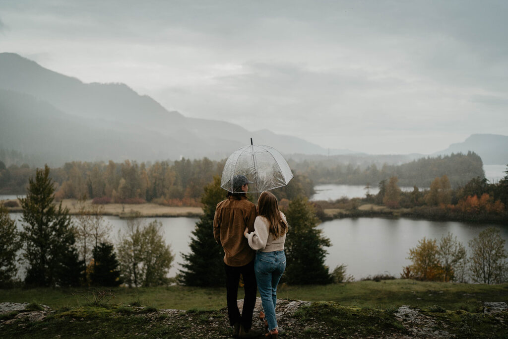 A couple cuddling under an umbrella during their Columbia River Gorge engagement. 