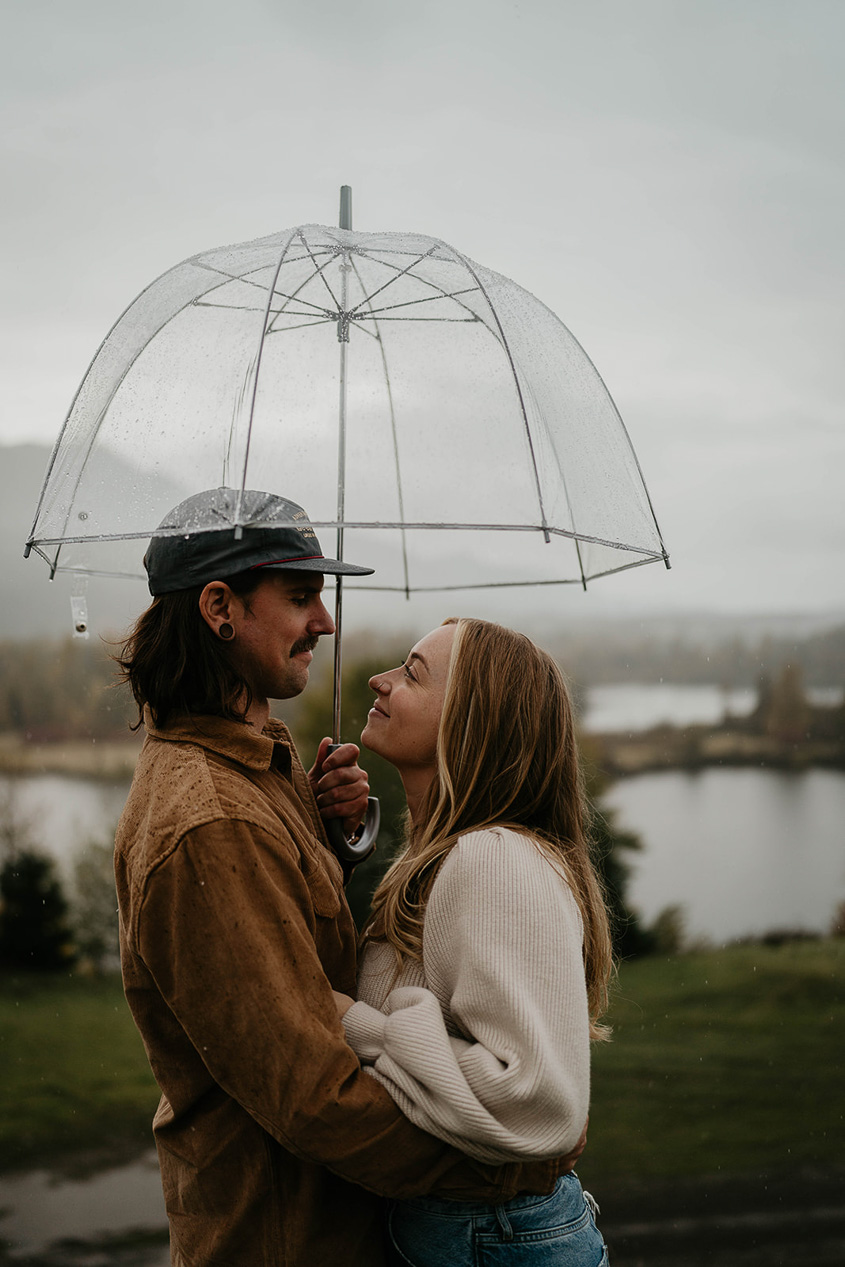 A couple staring lovingly into each other's eyes under an umbrella during a gloomy day at the Columbia River Gorge.