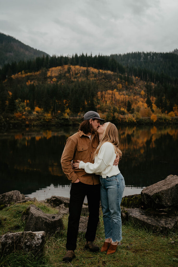A couple kissing with the Columbia river and evergreen trees in the background. 