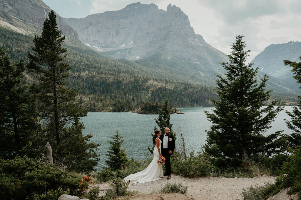 The newlyweds standing close with a lake and mountain in the background. 