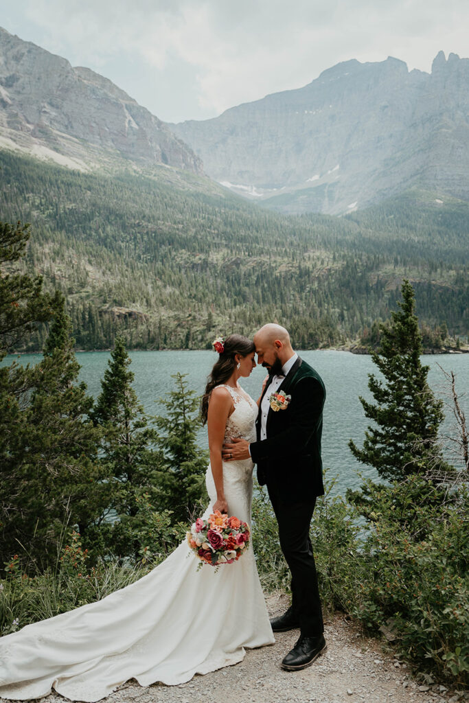 The newlyweds standing close with a lake and mountain in the background. 