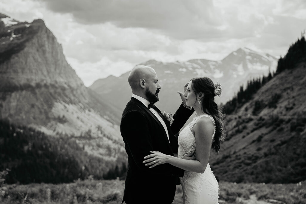 The couple holding each other close with large mountains surrounding them. 