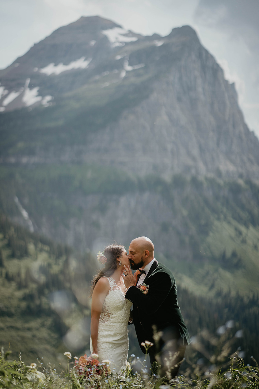 The newlyweds kissing with large mountains surrounding them during their Glacier National Park elopement. 