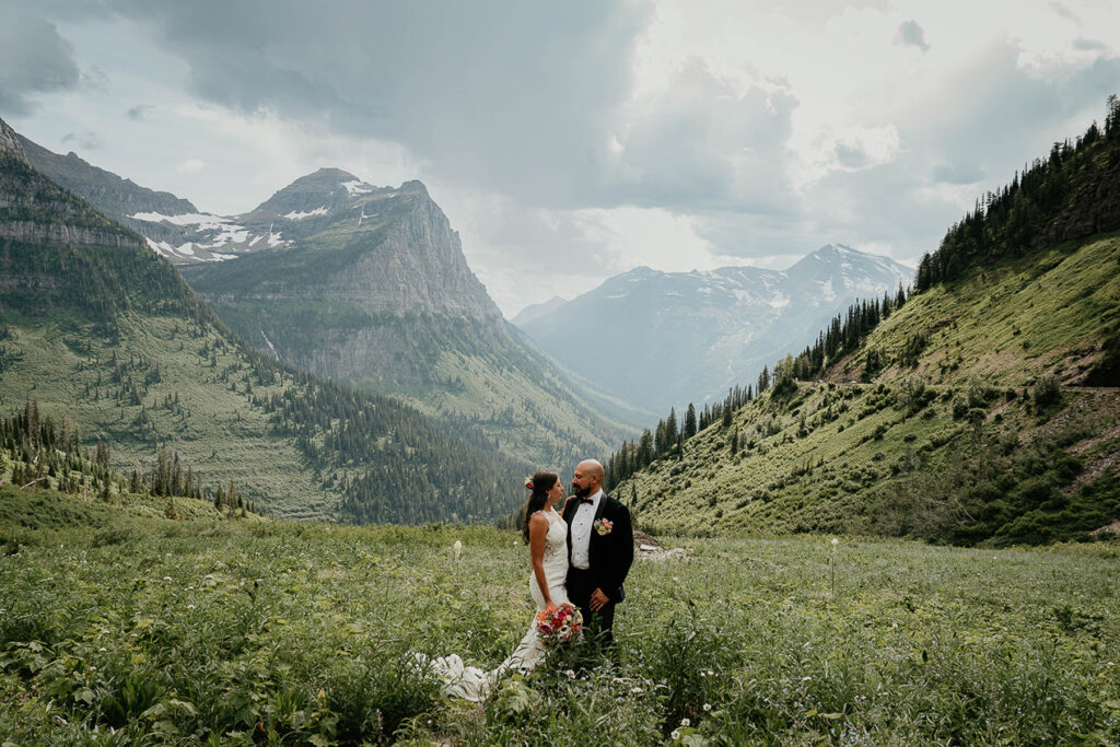 The couple standing in a field with large trees and mountains in the background during their Glacier National Park Elopement. 