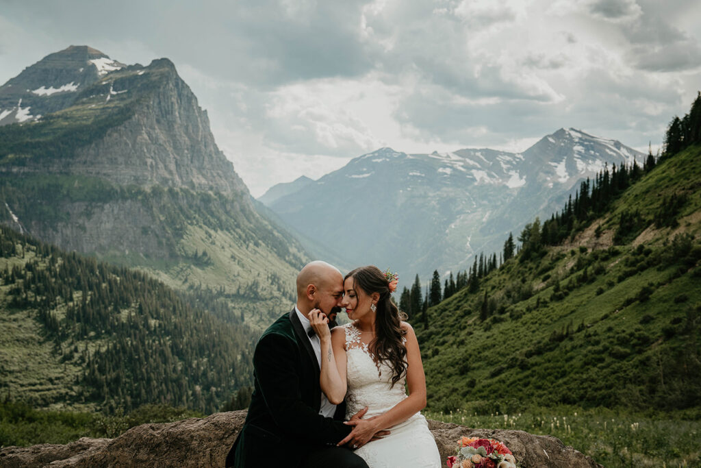 the newlyweds sitting on a rock and embracing each other with large mountains surrounding them. 