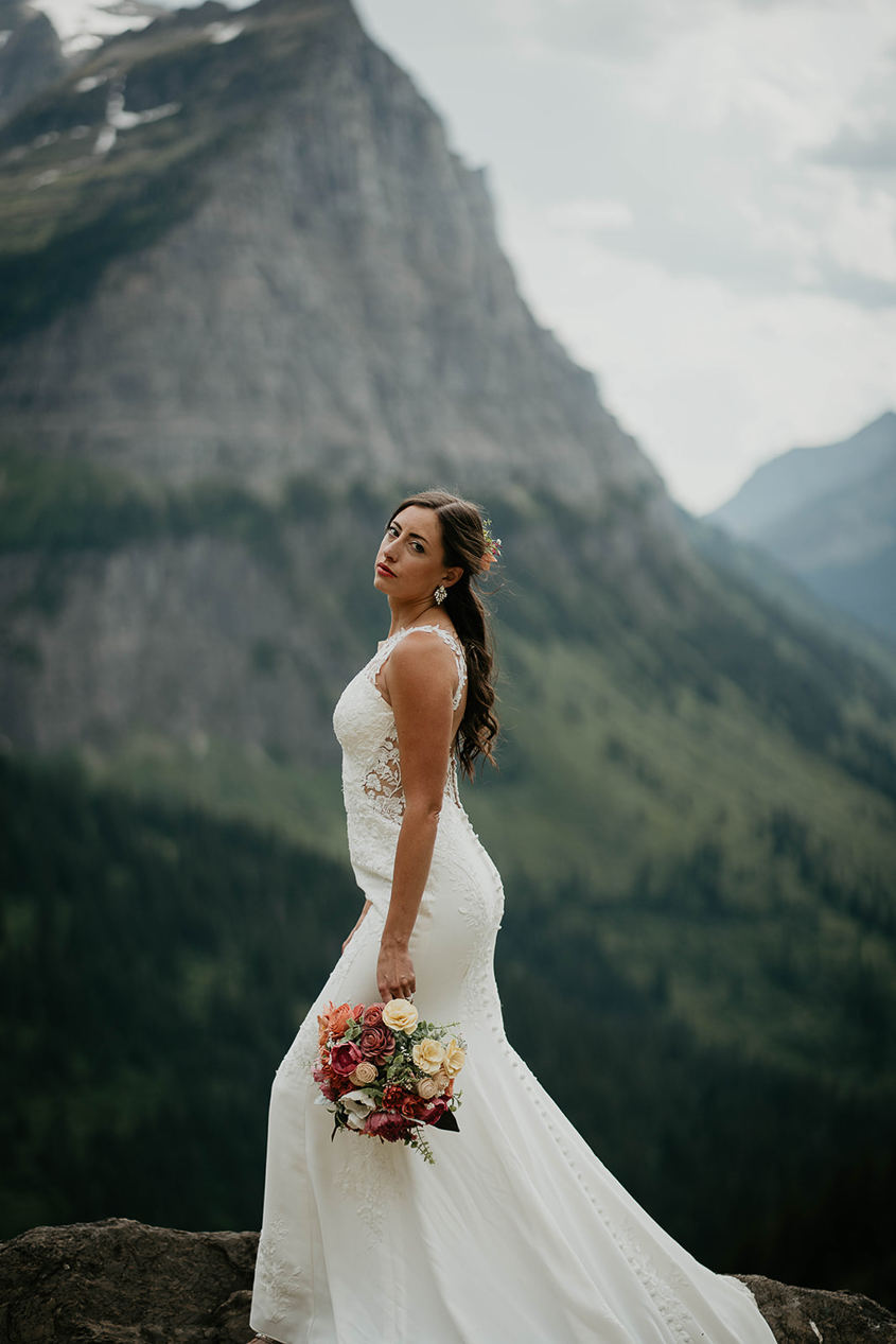 The bride posing seriously while holding a bouquet of flowers in Glacier National Park. 