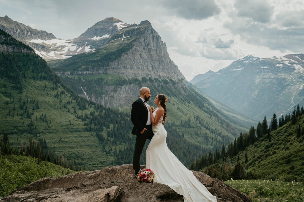 The couple holding each other with large mountains in the background. 