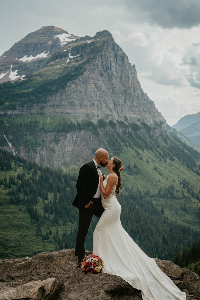The couple kissing with a large mountain behind them during their Glacier National Park elopement. 