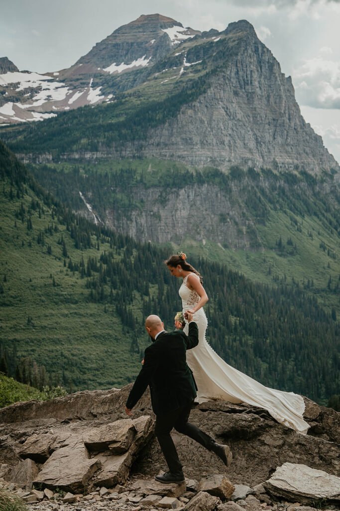 The couple holding hands with a large mountain behind them during their Glacier National Park elopement. 