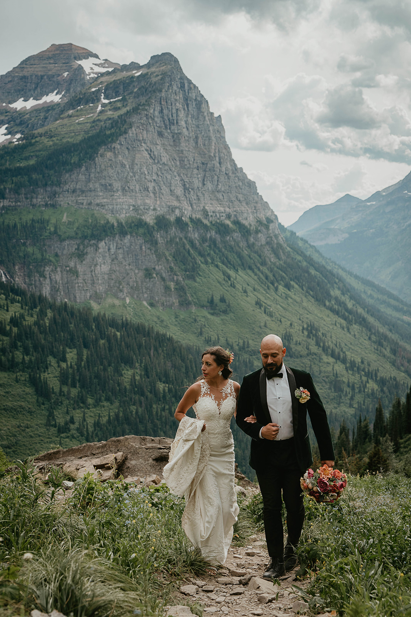 The couple hiking up a trail with a large mountain behind them during their Glacier National Park elopement. 
