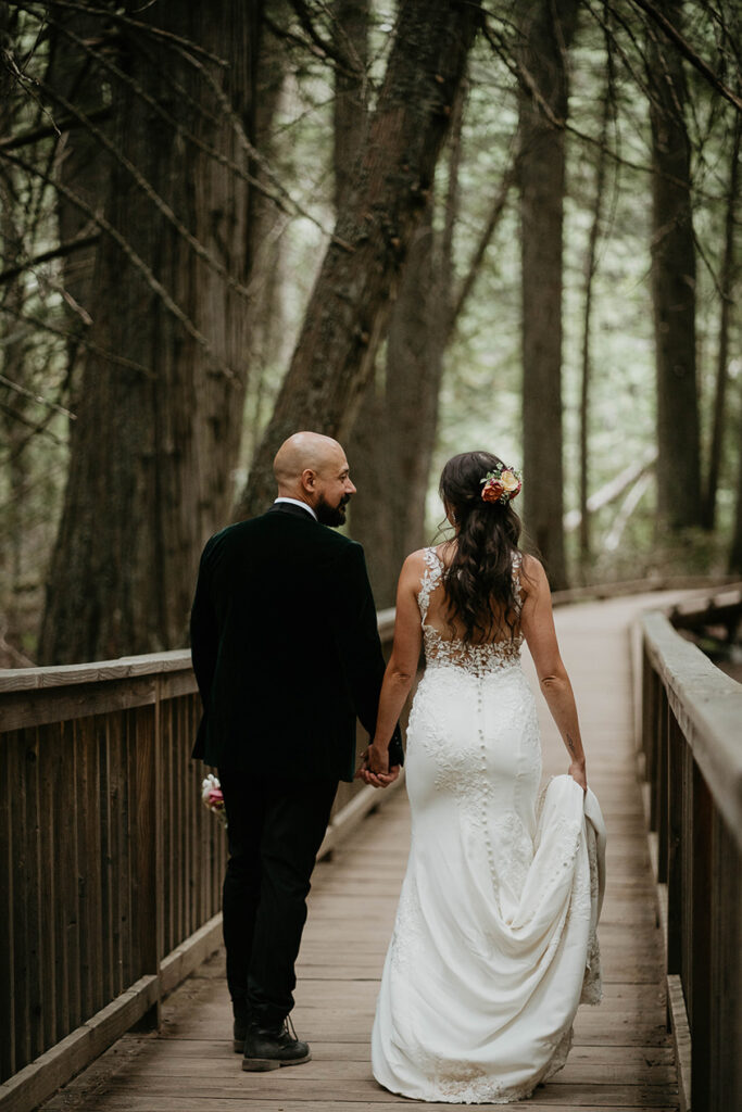 the couple walking across a wooden bridge in the middle of a forest. 