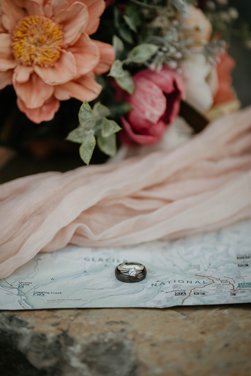 A map, bridal veil, flower bouquet, and wedding rings on a rock. 