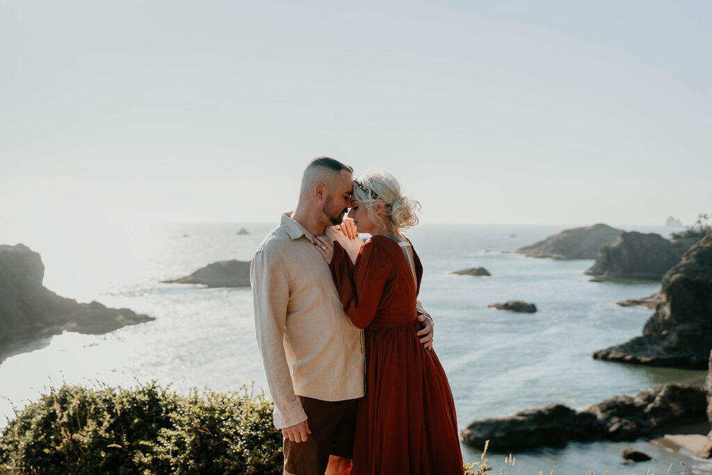 A newlywed couple holding each other with the pacific ocean in the background. 