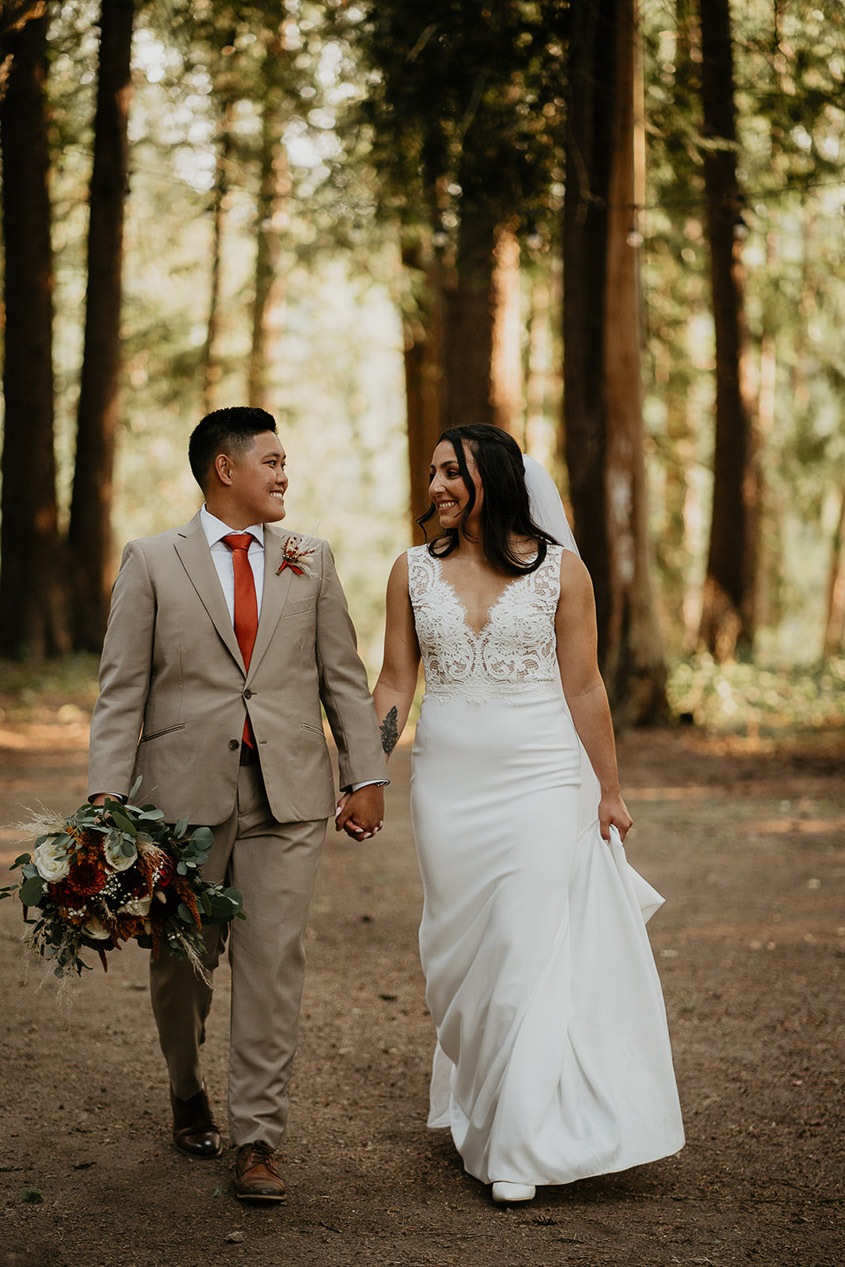 A newlywed couple walking down a trail in the middle of the forest. 