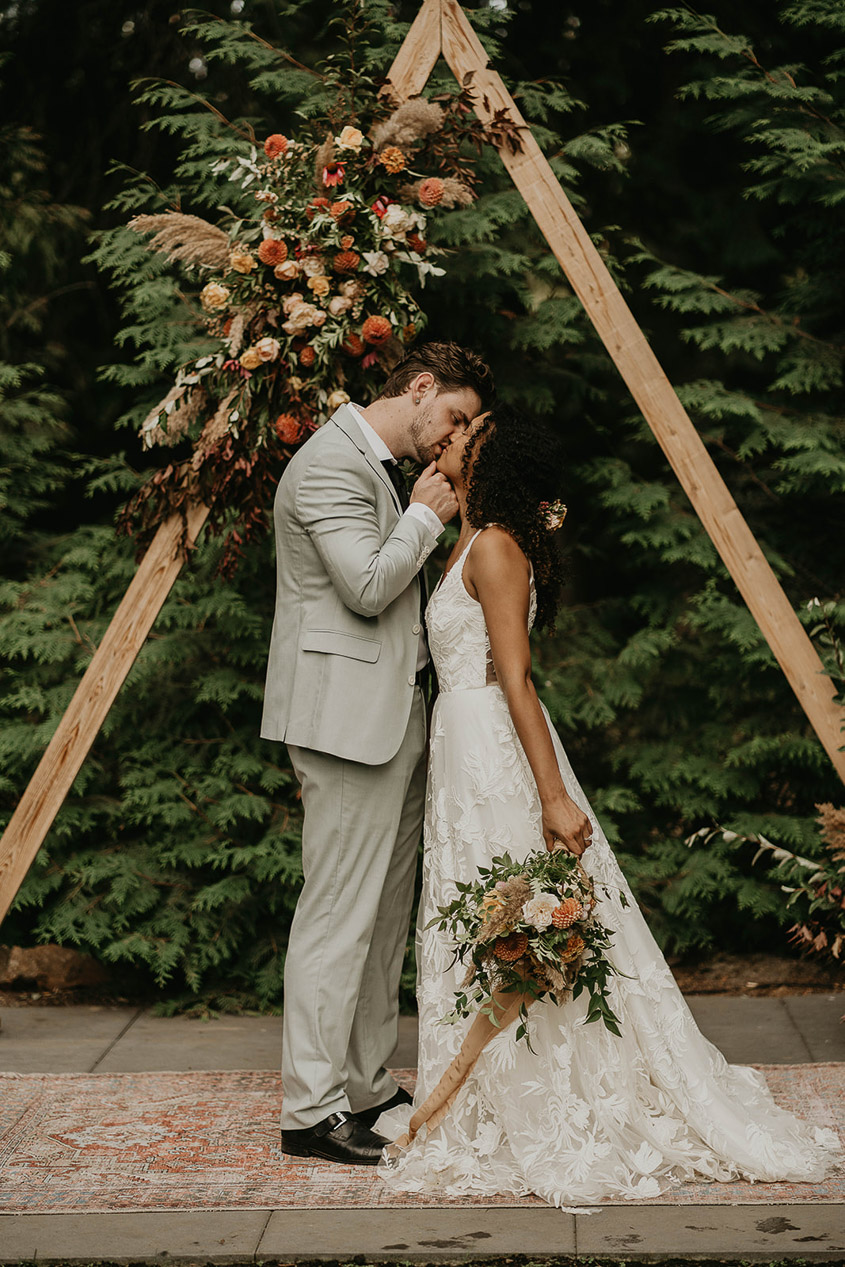 Newlyweds kissing with a wooden triangle decoration in the background.