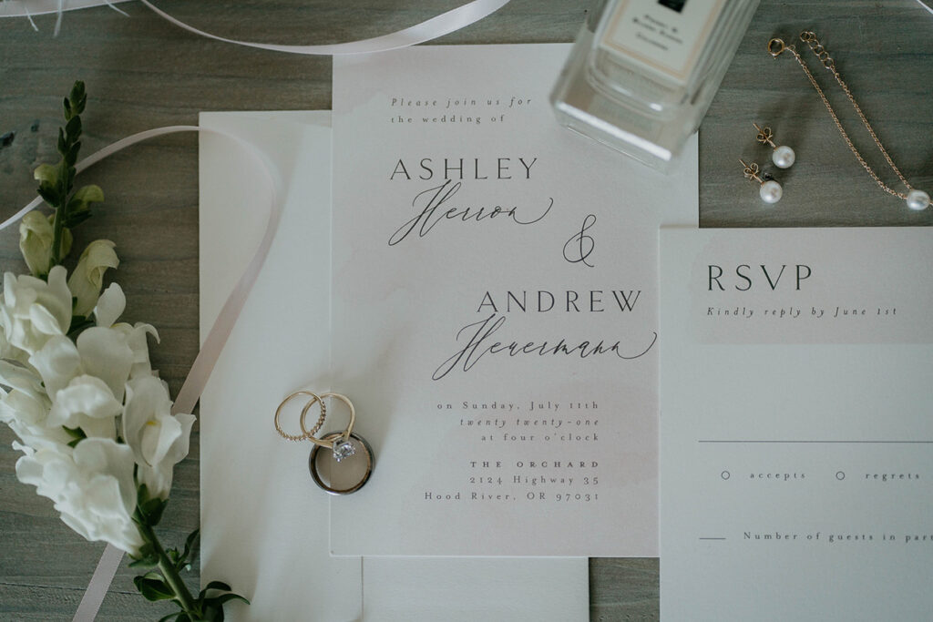 a flat lay with the wedding invite, rings and other jewelry, and flowers. 