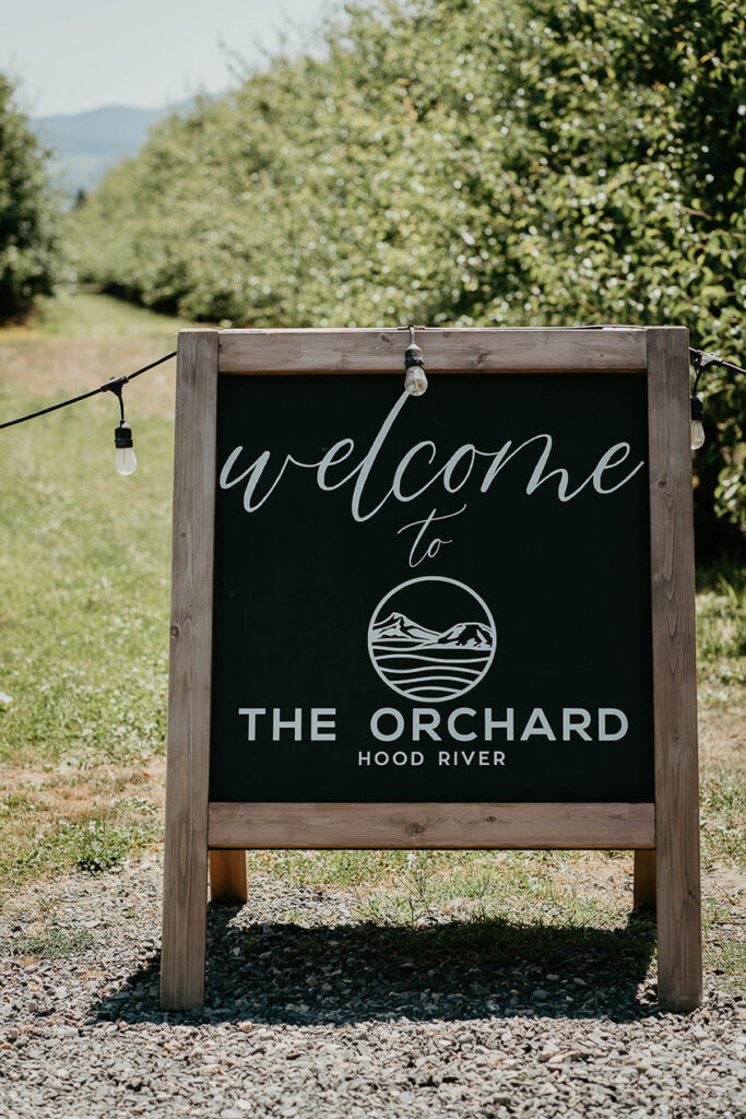 A sign that reads "welcome to The Orchard Hood River" with a row of trees in the background. 
