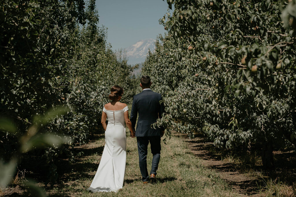 The bride and groom walking through a grove of trees at The Orchard Hood River. 