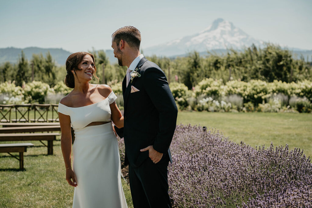 The bride and groom smiling at each other with flowers and Mt. Hood in the background. 