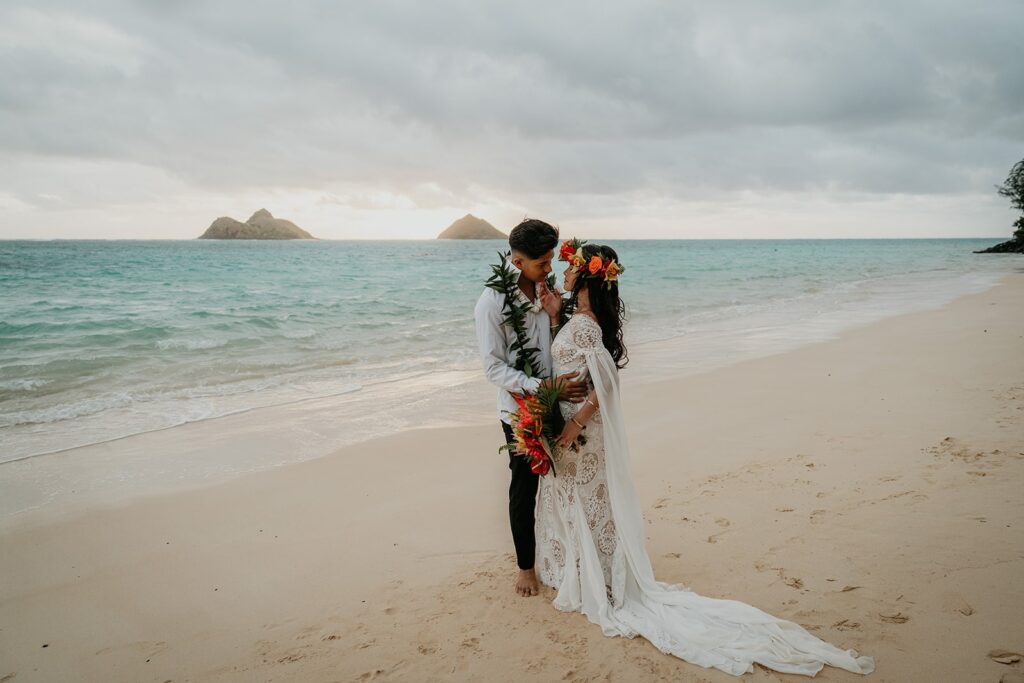 Bride and groom kiss on a white sand beach during their elopement in Oahu