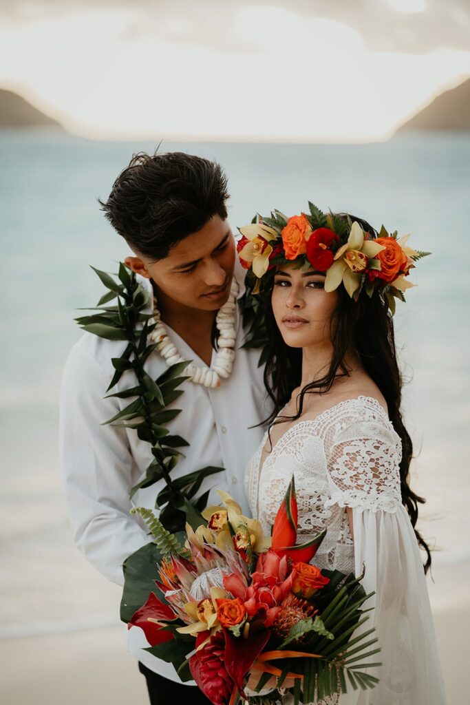 Bride wears a red and orange floral crown during her beach elopement in Oahu
