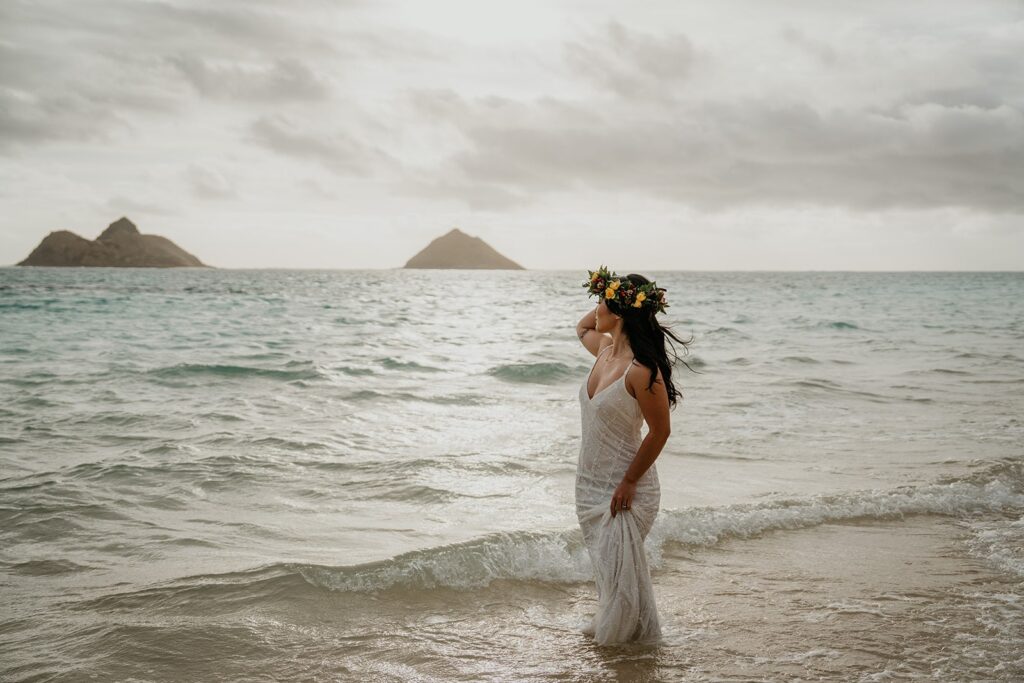 Bride stands in the ocean in her wedding dress while she elopes in Hawaii