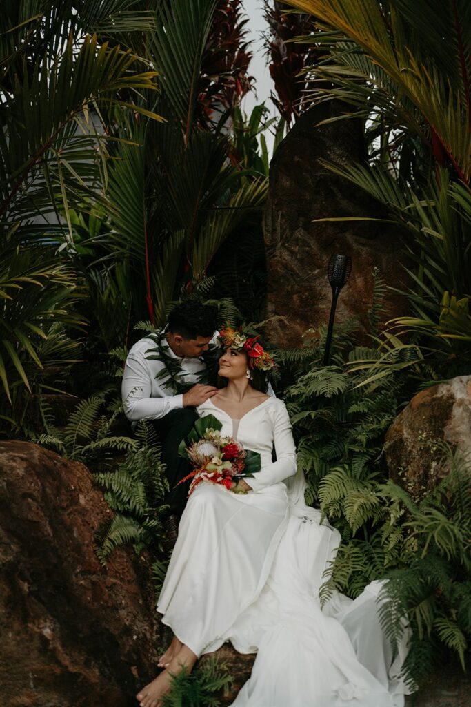 Bride and groom sit in a tropical rainforest after they elope in Hawaii
