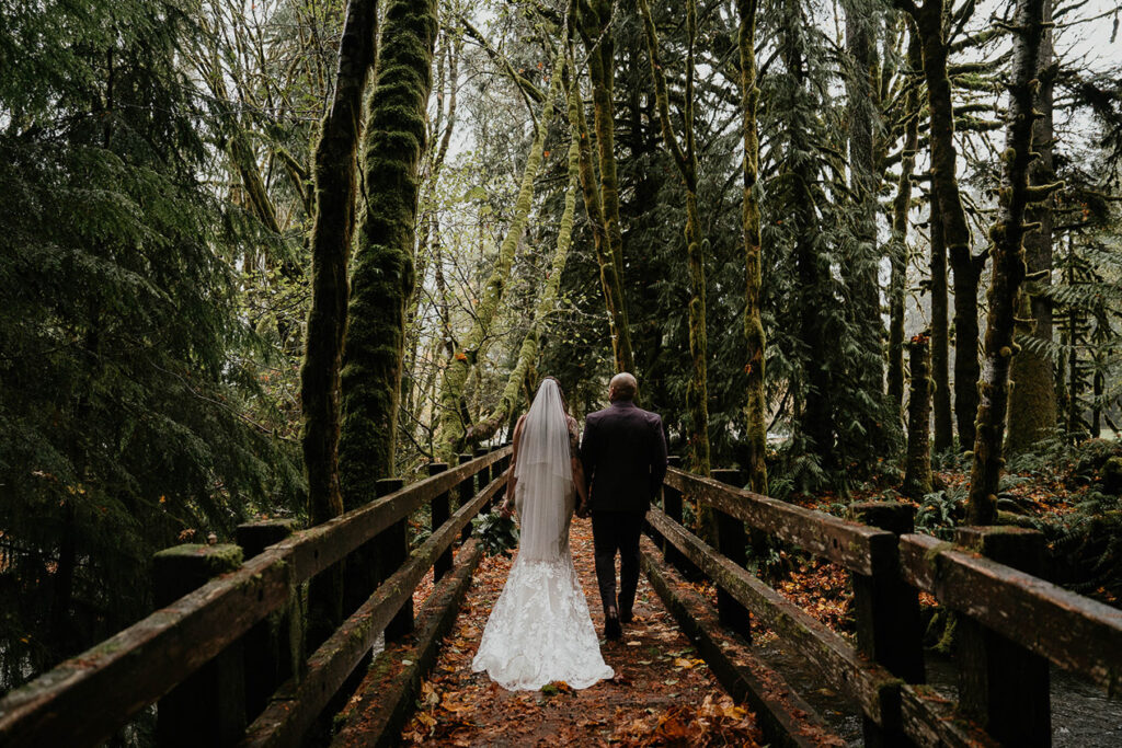 The bride and groom walking on a bridge in the forest. 