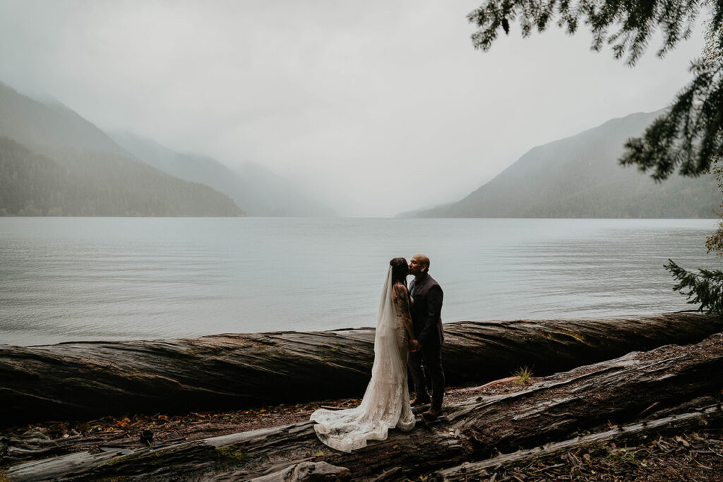 The newlyweds kissing on a log by Lake Crescent.