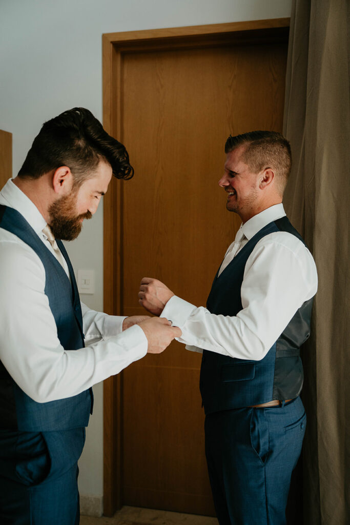 A groomsman helping add cufflinks to the groom's suit. 