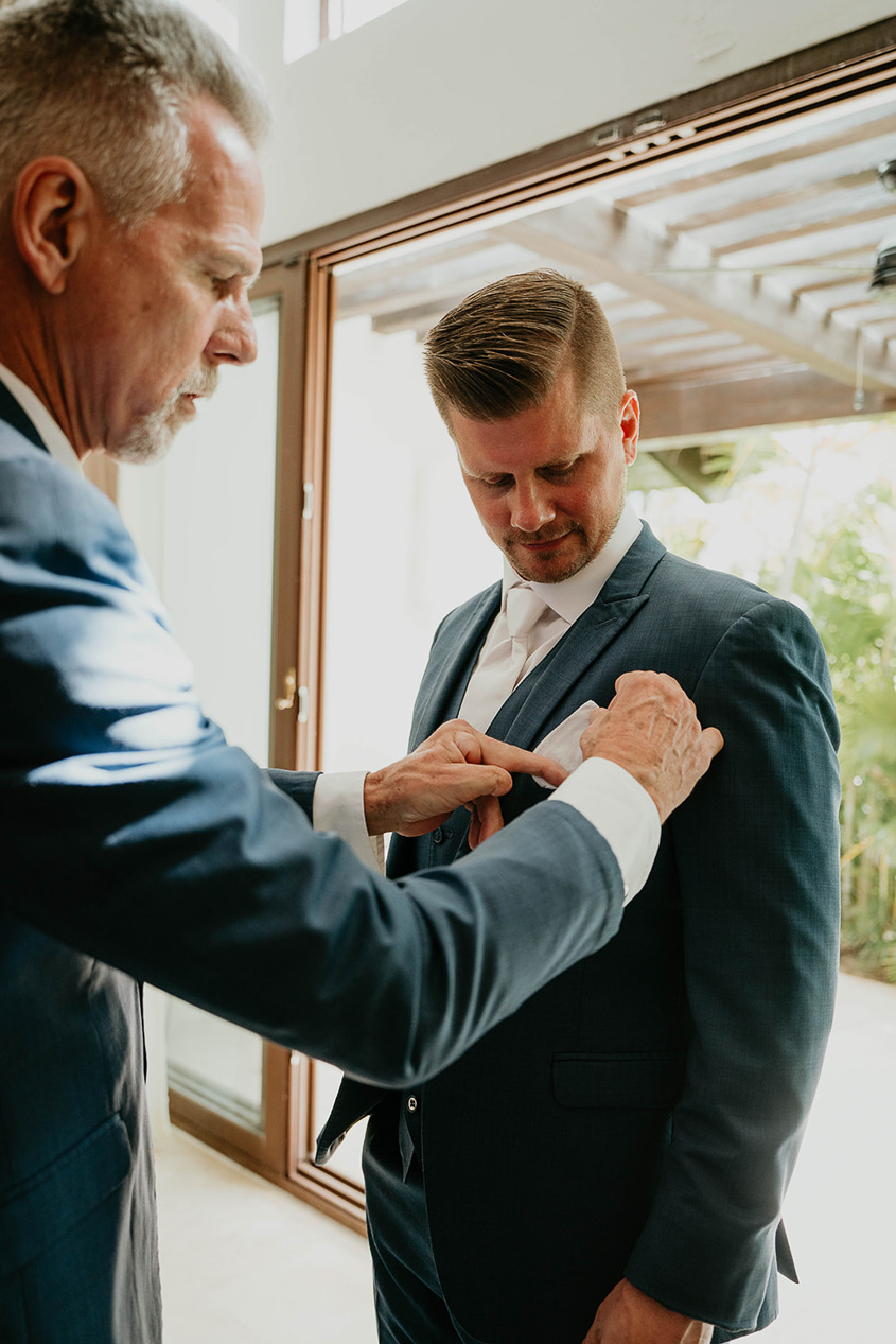 The bride's father adding a pocket square to the groom's suit. 