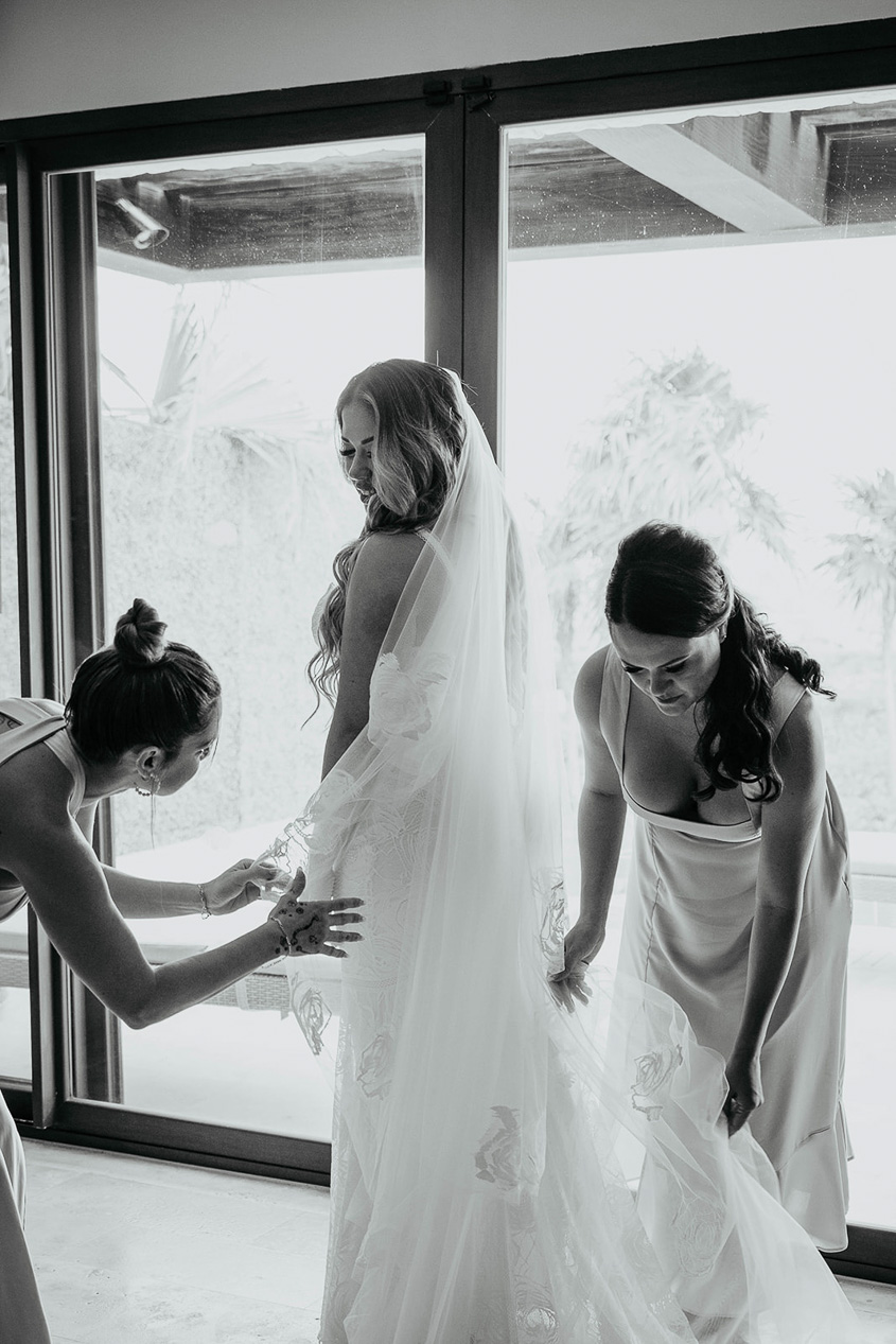 Bridesmaids helping the bride put on her dress. 