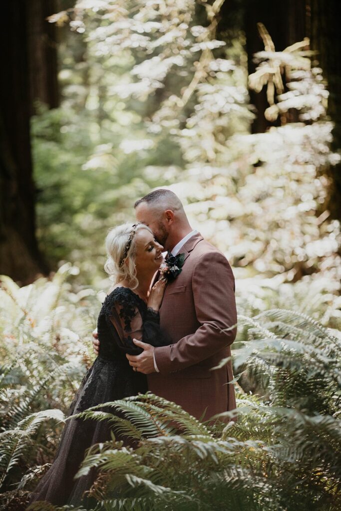 Bride and groom kiss in front of a redwood tree during their forest elopement on the Oregon Coast