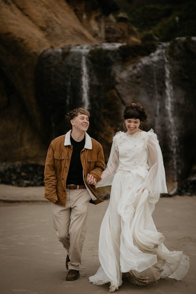 Bride and groom hold hands while running across the beach during their Oregon Coast elopement