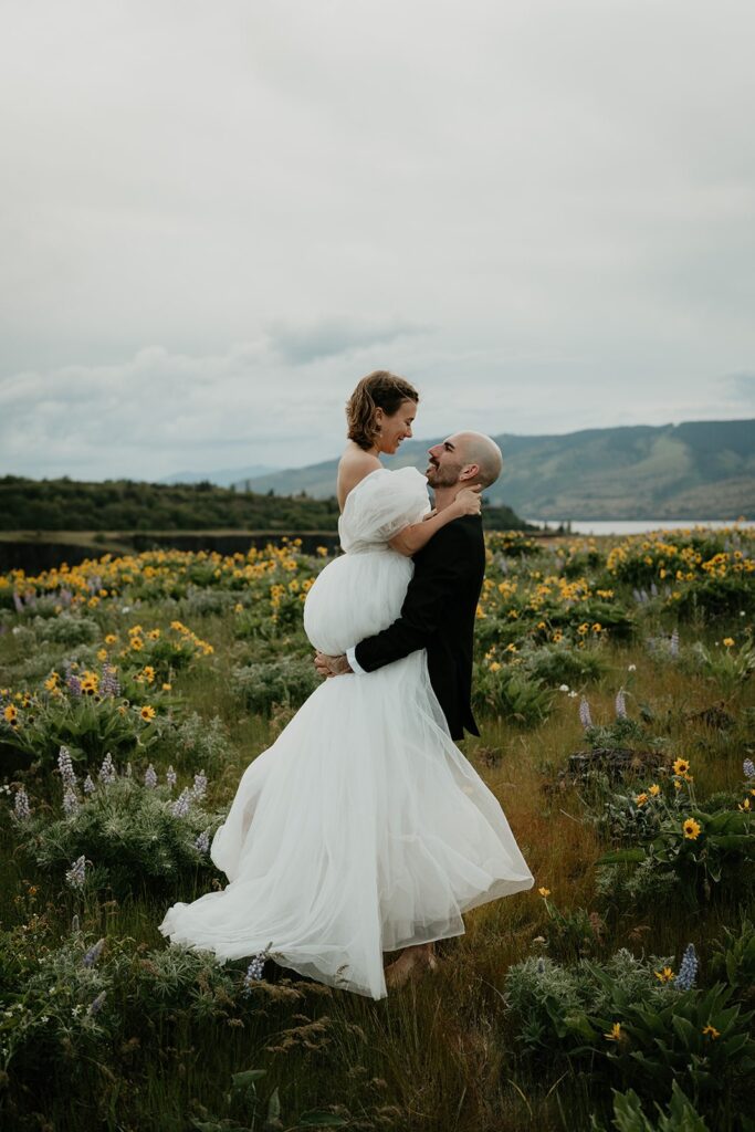 Groom picks bride up while standing in a wildflower field in the Columbia River Gorge