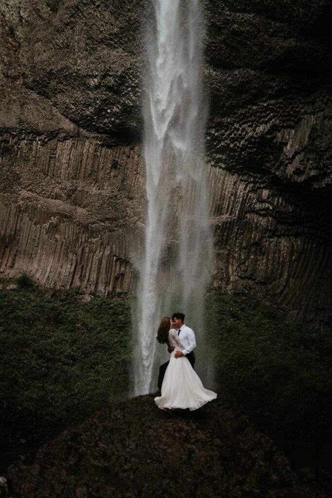 Bride and groom hug in front of a waterfall during their Columbia River Gorge elopement in the PNW