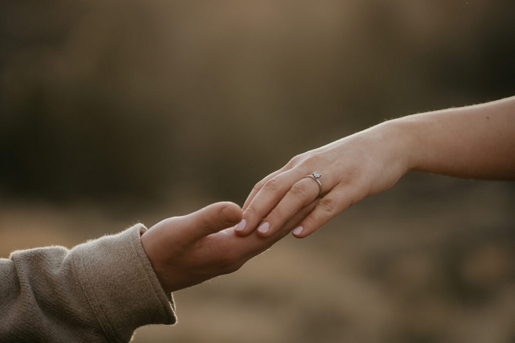 A couple touching hands, showcasing the soon-to-be bride's engagement ring. 