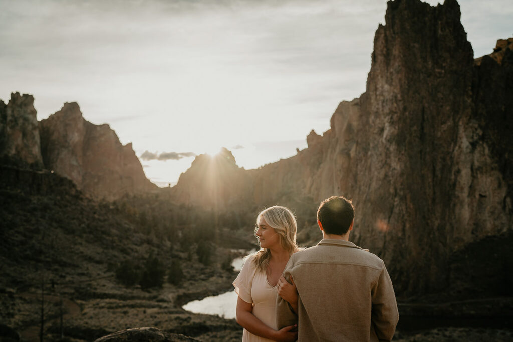 a couple holding each other with rivers and spires in the background during their Smith Rock engagement session. 